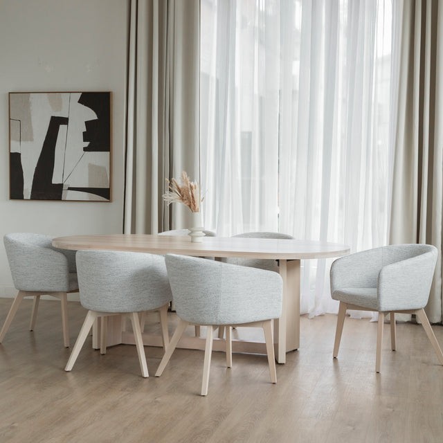 Table ovale en bois clair avec chaises crème modernes dans salle a manger lumineuse.