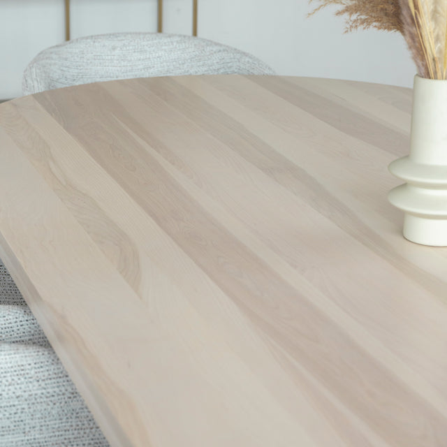 Table ovale en bois clair avec chaises crème modernes dans salle a manger lumineuse.