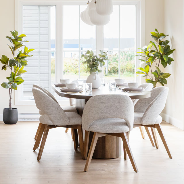 Salle a manger lumineuse avec table ronde en bois et chaises beige devant grande fenetre.