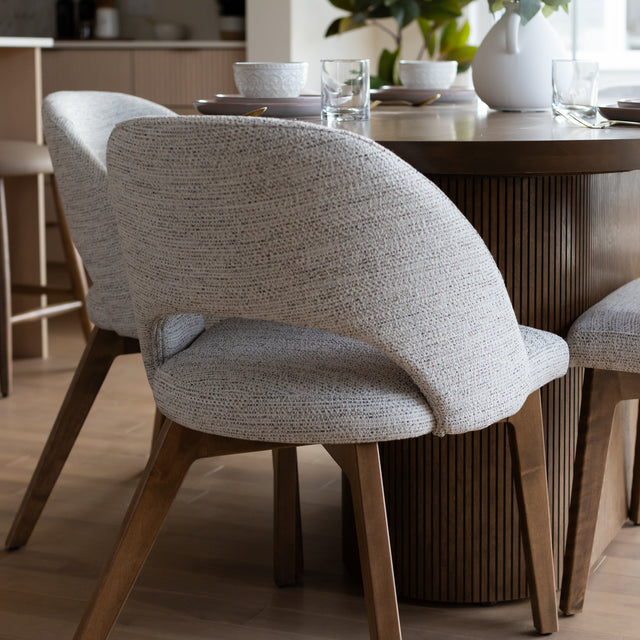 Gros plan sur chaise beige en tissu devant table ronde en bois a base rainuree.