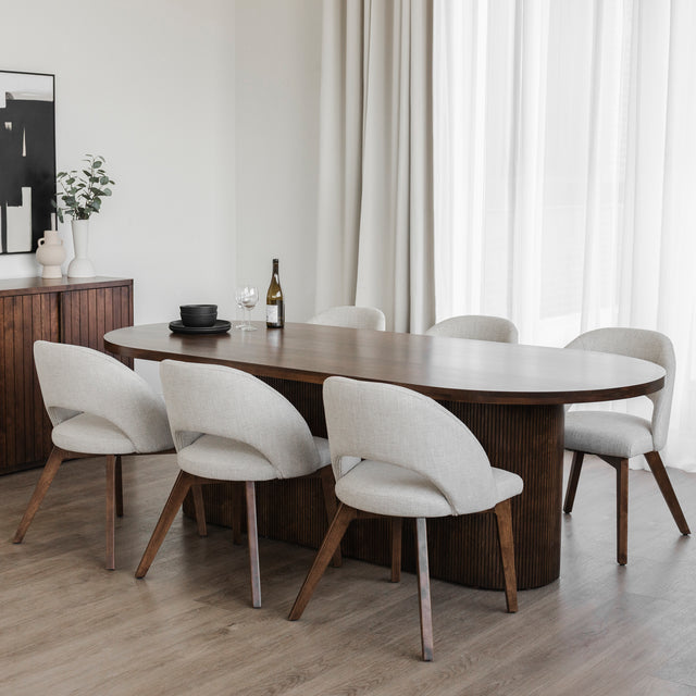 Salle a manger moderne avec table ovale en bois fonce et chaises beige sur plancher clair.