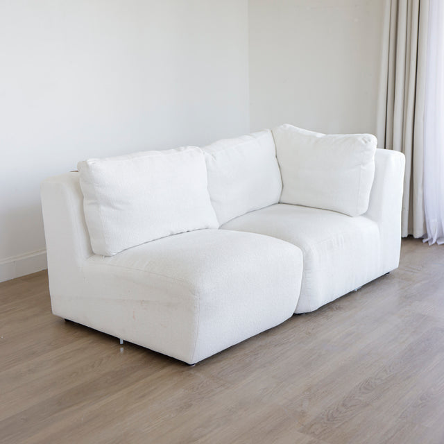 Canape d’angle blanc en tissu bouclette avec assises profondes et coussins moelleux sur parquet clair.