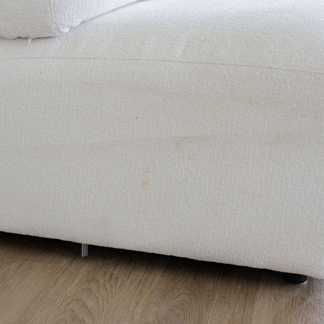 Detail du tissu bouclette blanc d’un canape moderne avec base reposee sur parquet clair.