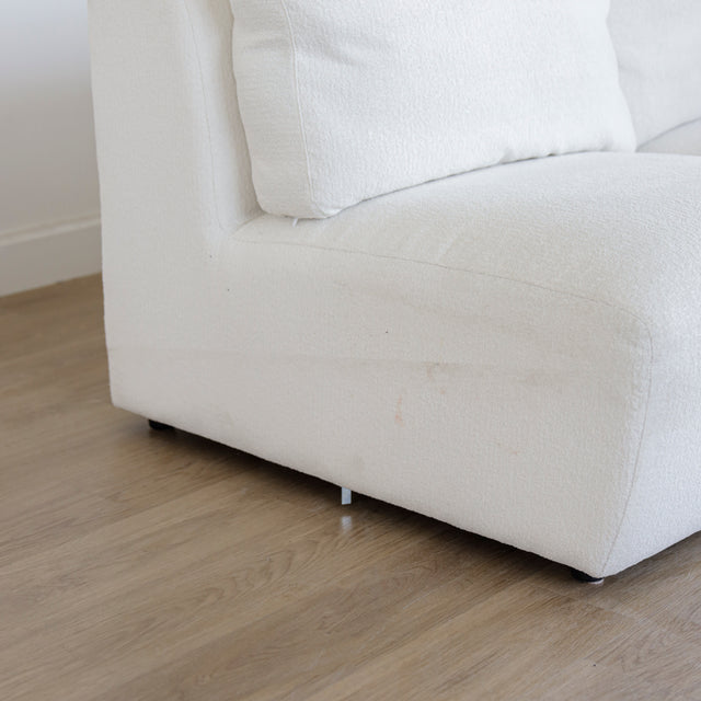 Angle inferieur d’un canape blanc en tissu bouclette avec base reposee sur parquet en bois clair.