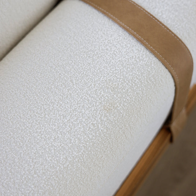 Gros plan sur le tissu bouclette blanc et detail de sangle en cuir camel d’un canape moderne.