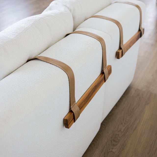 Dossier de canape blanc en tissu bouclette avec sangles decoratives en cuir et barres en bois clair.