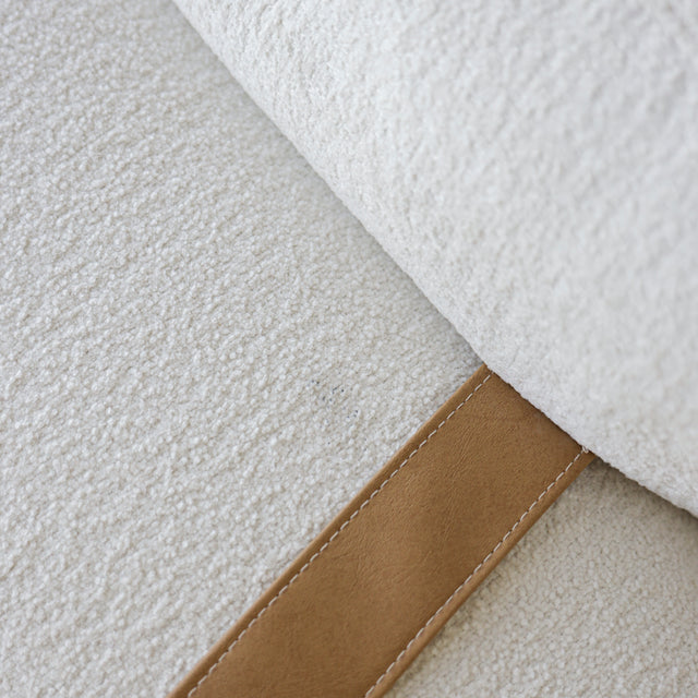 Gros plan sur le tissu bouclette blanc et detail de sangle en cuir camel d’un canape moderne.