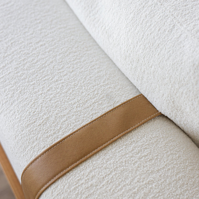 Gros plan sur le tissu bouclette blanc et detail de sangle en cuir camel d’un canape moderne.