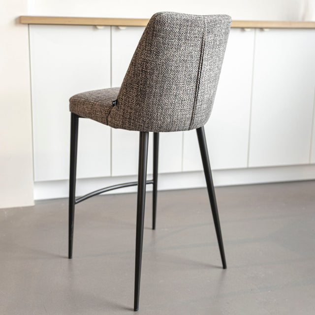 Tabouret de bar design avec assise en tissu brun/gris et pieds en metal noir, ideal pour cuisine moderne.