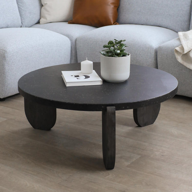 Table basse ronde noire avec pieds en bois fonce devant canape gris clair.