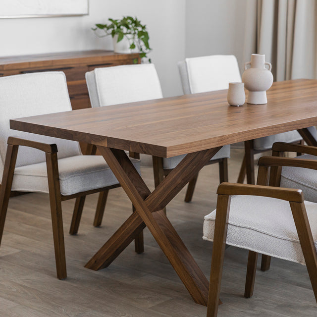 Table en bois noyer avec pieds en croix assortis et chaises blanches au cadre en bois, dans une salle à manger au style moderne et chaleureux.