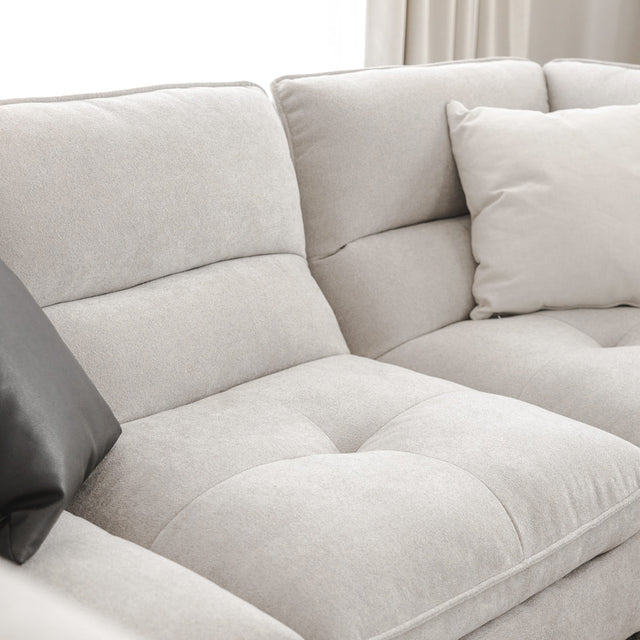 Vue rapprochée d’un canapé sectionnel gris clair avec coussins noirs et beiges, mettant en valeur la texture douce et les coutures du tissu.