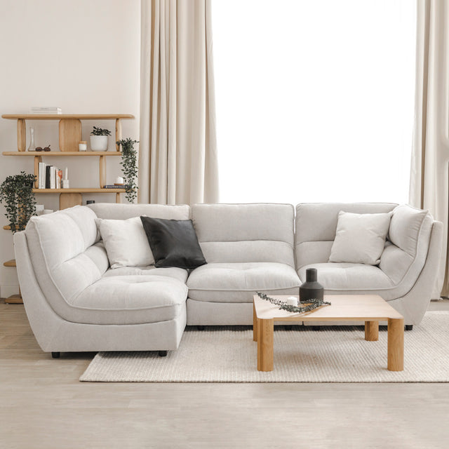 Canapé sectionnel gris clair moderne avec coussins noirs et blancs, table basse en bois et étagère décorative en arrière-plan.