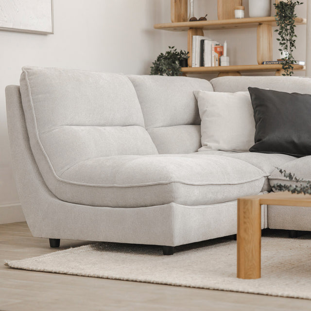 Angle du canape sectionnel gris clair avec coussins noirs et blancs, table basse en bois et decor vegetal.