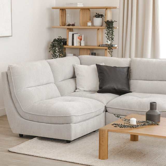 Canapé sectionnel gris clair moderne avec coussins noirs et blancs, table basse en bois et étagère décorative en arrière-plan.