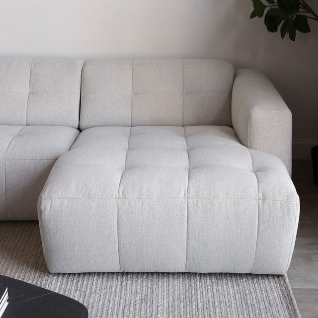 Canape d angle beige clair avec assise large et matelassee sur tapis texture gris.