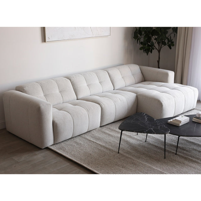 Canape d angle beige clair matelasse au style contemporain sur tapis gris clair.