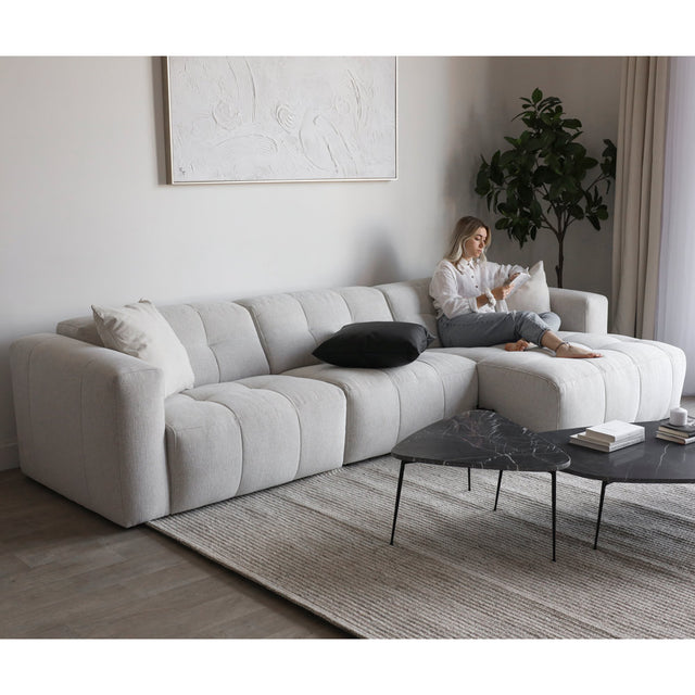 Salon moderne avec canape d angle beige clair matelasse et table basse noire en marbre.