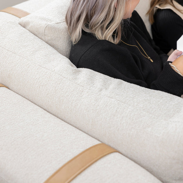 dos de canape beige clair avec sangles en cuir beige et personne assise lisant.