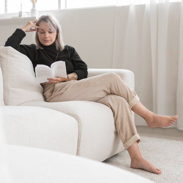 canape beige clair en tissu boucle avec personne assise lisant un livre.