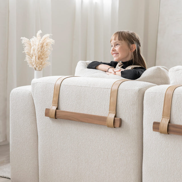 dos de canape beige clair avec sangles en cuir et barres en bois, enfant appuyee sur le dossier.