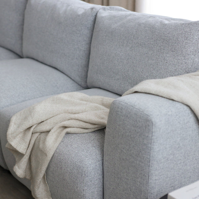 canape gris clair en tissu avec plaid beige drape sur l accoudoir.