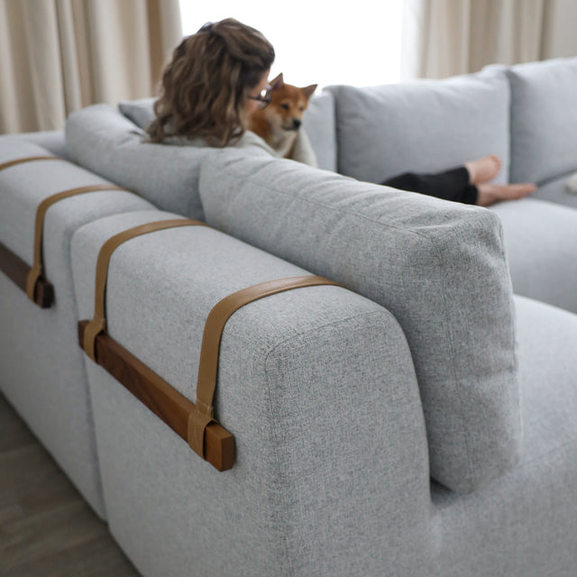 dos de canape gris clair avec sangles en cuir et barres en bois, personne assise avec chien.