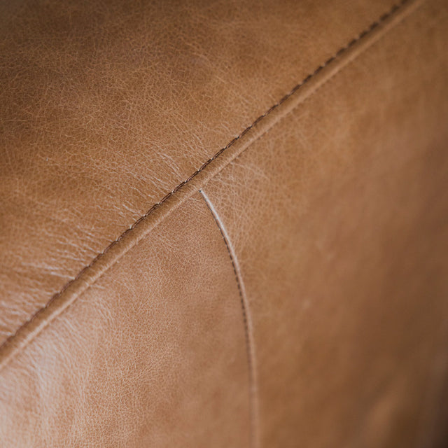 gros plan sur la texture et les coutures d’un canapé en cuir brun, mettant en valeur son grain naturel et ses finitions soignées.