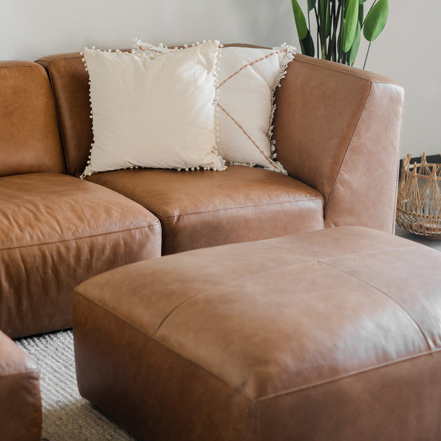 gros plan sur un canapé d’angle en cuir brun avec de grands coussins décoratifs beiges et une table basse assortie au premier plan.