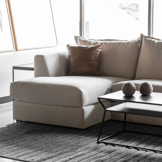 canape beige clair avec coussin brun et table basse noire sur tapis gris.