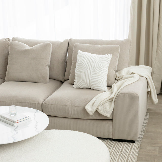 Canape beige en velours cotele avec coussins creme et plaid, table basse blanche moderne.