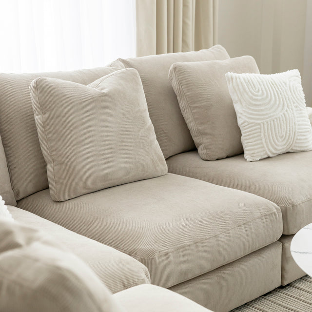 Canape beige en velours cotele avec coussins decoratifs creme sur fond lumineux.