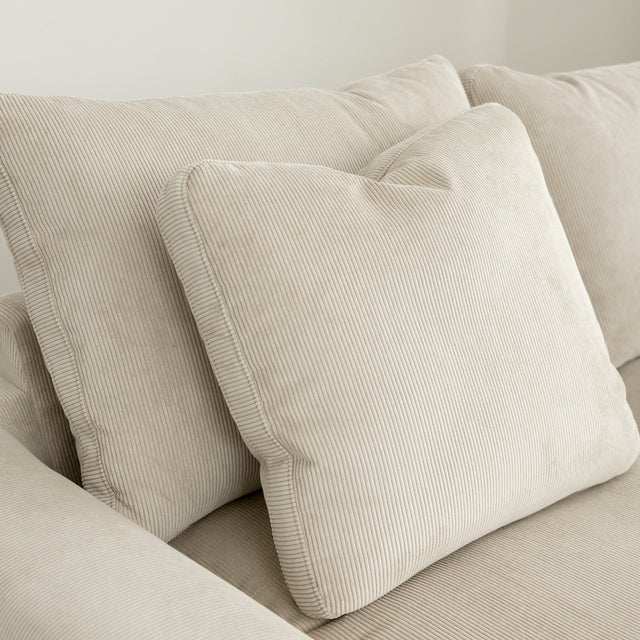 Coussins beiges en velours cotele sur canape moderne et confortable.