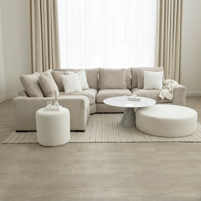 Salon elegant avec canape beige en velours cotele, table basse blanche et pouf en bouclette sur tapis clair.