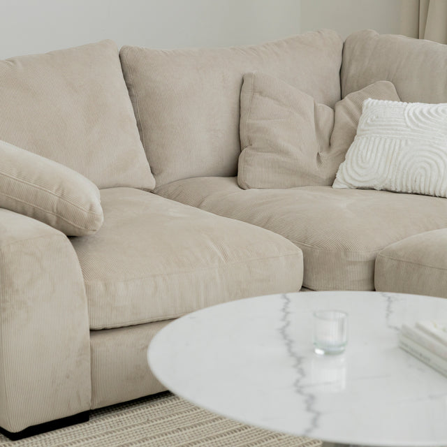 Canape d angle beige en velours cotele avec coussins creme et table basse blanche en marbre.