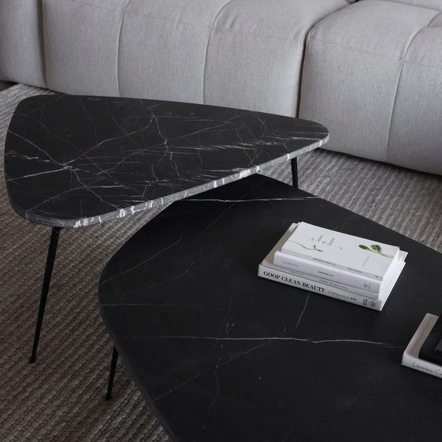 Gros plan sur deux tables basses en marbre noir veine blanche avec pieds fins metalliques.