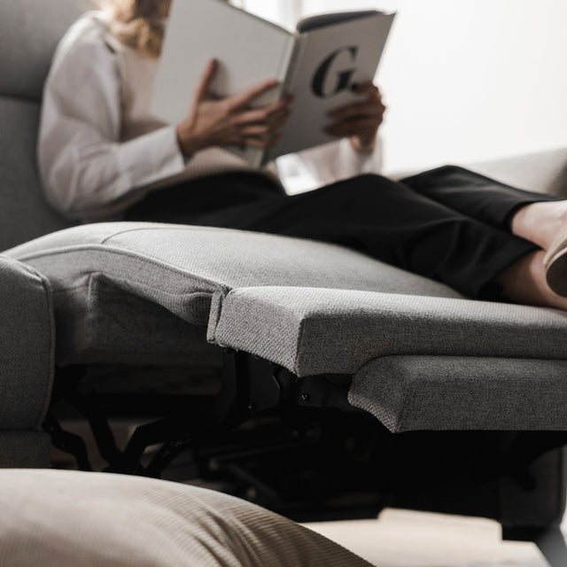 assise relax du canape clair avec repose pieds ouvert et personne lisant confortablement.