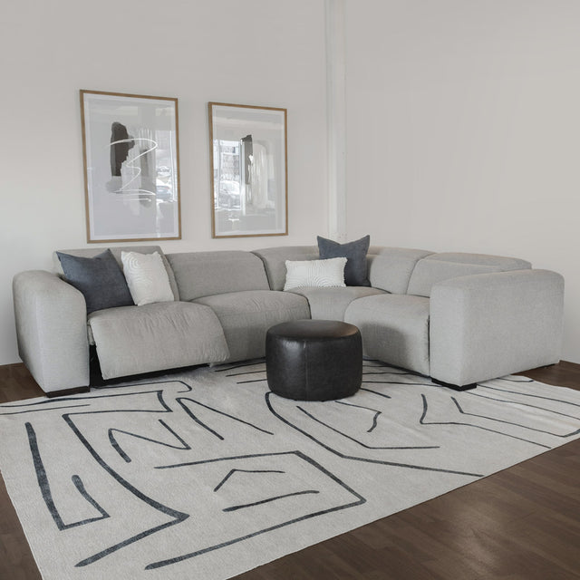 canape d angle gris clair avec coussins bleus et pouf noir sur tapis moderne.