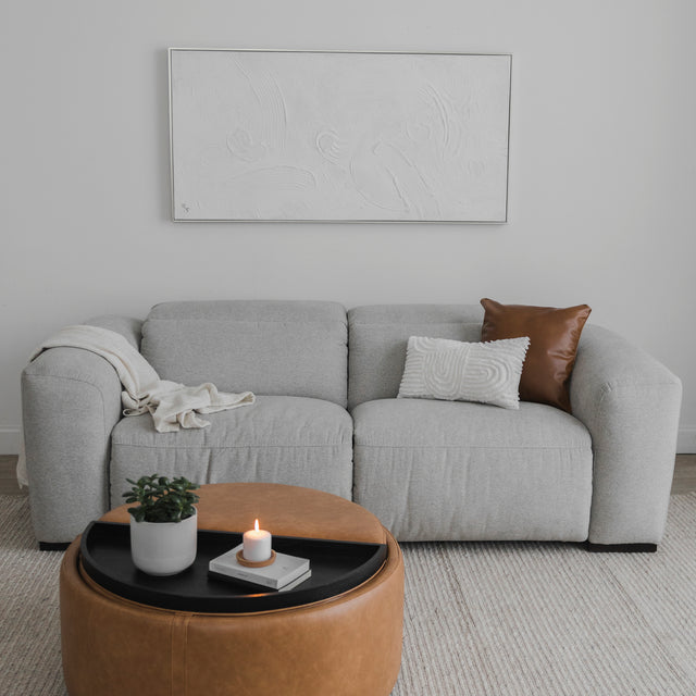 canape gris clair deux places avec coussins decoratifs et table ronde en cuir dans salon minimaliste.