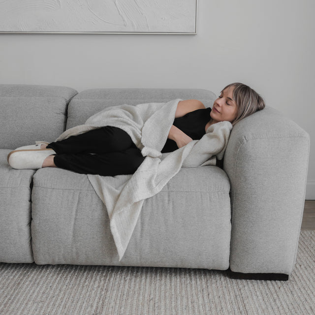 canape gris clair confortable avec femme detendue allongee sous un plaid dans salon epure.