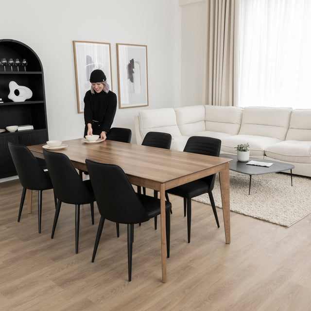 Table a manger en bois naturel avec six chaises noires dans salon moderne et lumineux.
