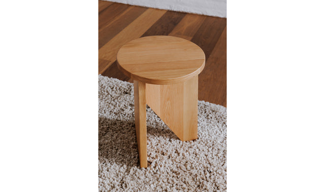 Table d'appoint en bois clair au design minimaliste pose sur tapis texture dans un interieur moderne.