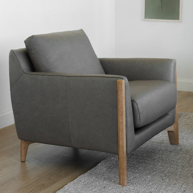 Fauteuil en cuir gris avec accoudoirs et pieds en bois clair au design moderne.
