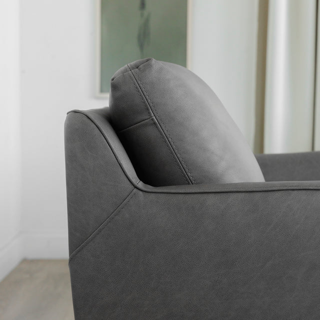 zoom sur le dossier capitonne du fauteuil en cuir gris avec couture detaillee.
