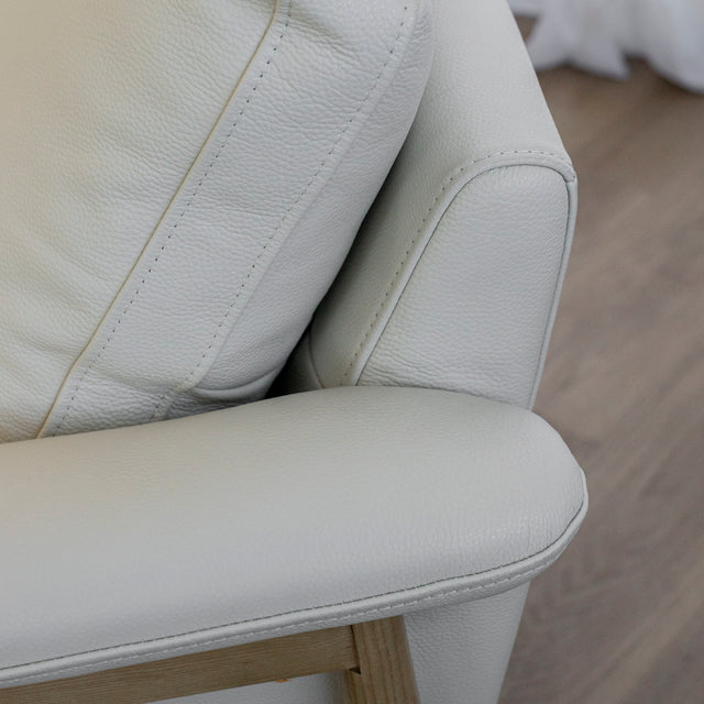 Image rapprochée d'un fauteuil en cuir crème avec structure en bois clair dans un salon lumineux.