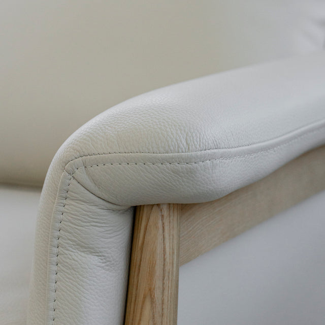 Image rapprochée d'un fauteuil en cuir crème avec structure en bois clair dans un salon lumineux.