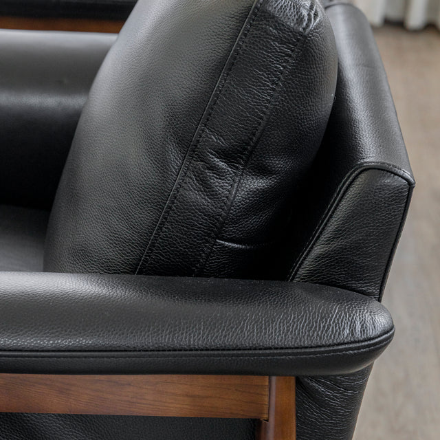Image rapprochée d'un fauteuil en cuir noir avec structure en bois dans un salon moderne.