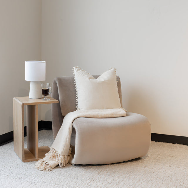 Fauteuil lounge beige avec coussin et jeté,dans un salon minimaliste.