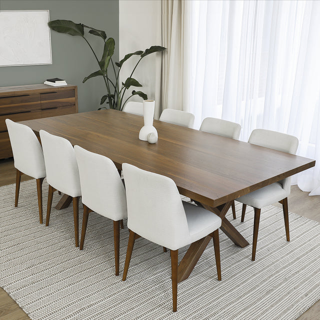Table en bois noyer avec pieds en croix et huit chaises blanches, dans une salle a manger elegante au style moderne.