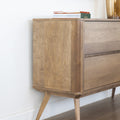 Buffet en bois clair style scandinave avec portes rainurées, pieds inclinés et déco minimaliste dans un salon moderne.